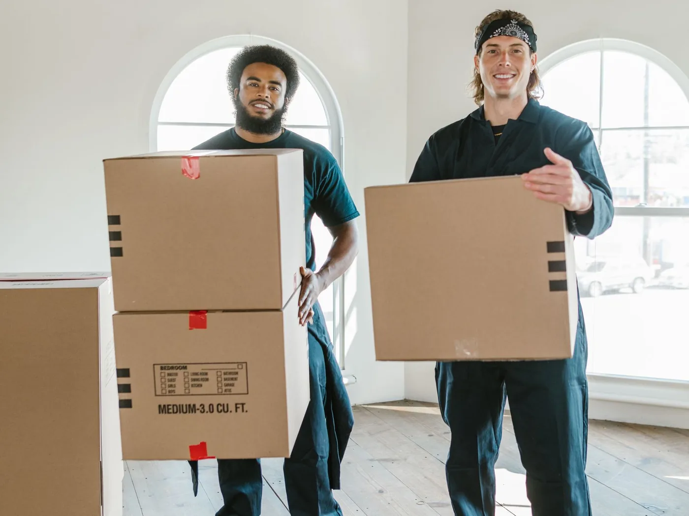 Zwei Umzugshelfer in Arbeitskleidung tragen Kartons in eine helle Wohnung